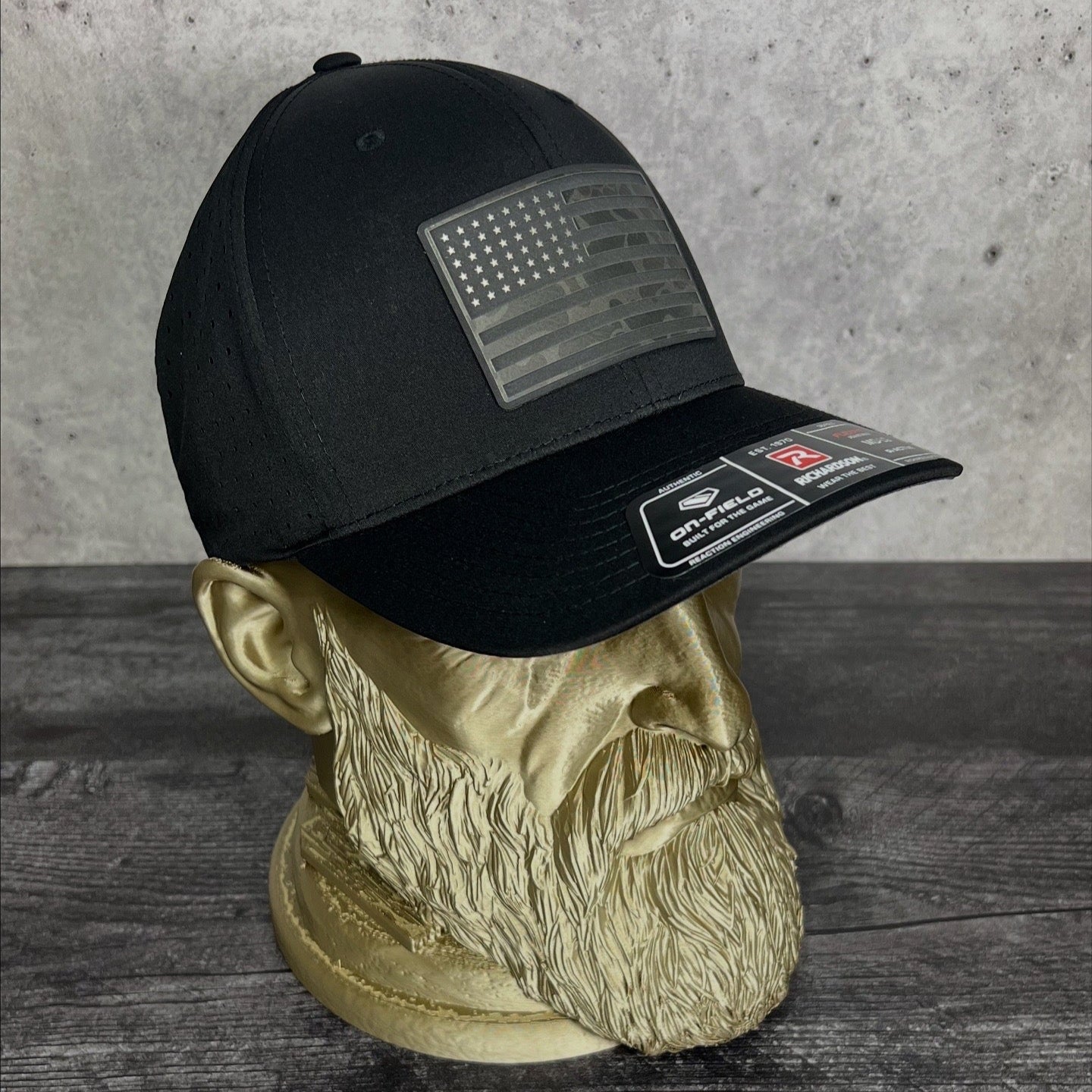 Black cap with American flag patch on a mannequin head against a gray background