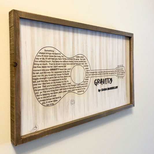 Framed acoustic guitar design with 'Gravity' by Sara Bareilles text on a white background