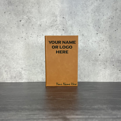 Brown leather notebook with customizable text on a gray surface and concrete wall background