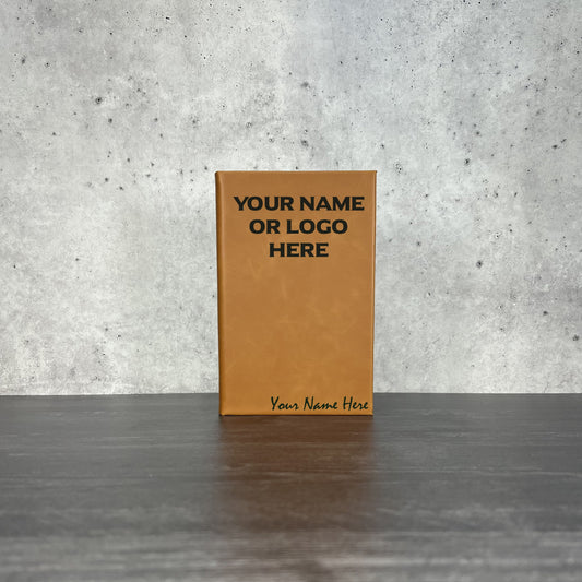 Brown leather notebook with customizable text on a gray surface and concrete wall background
