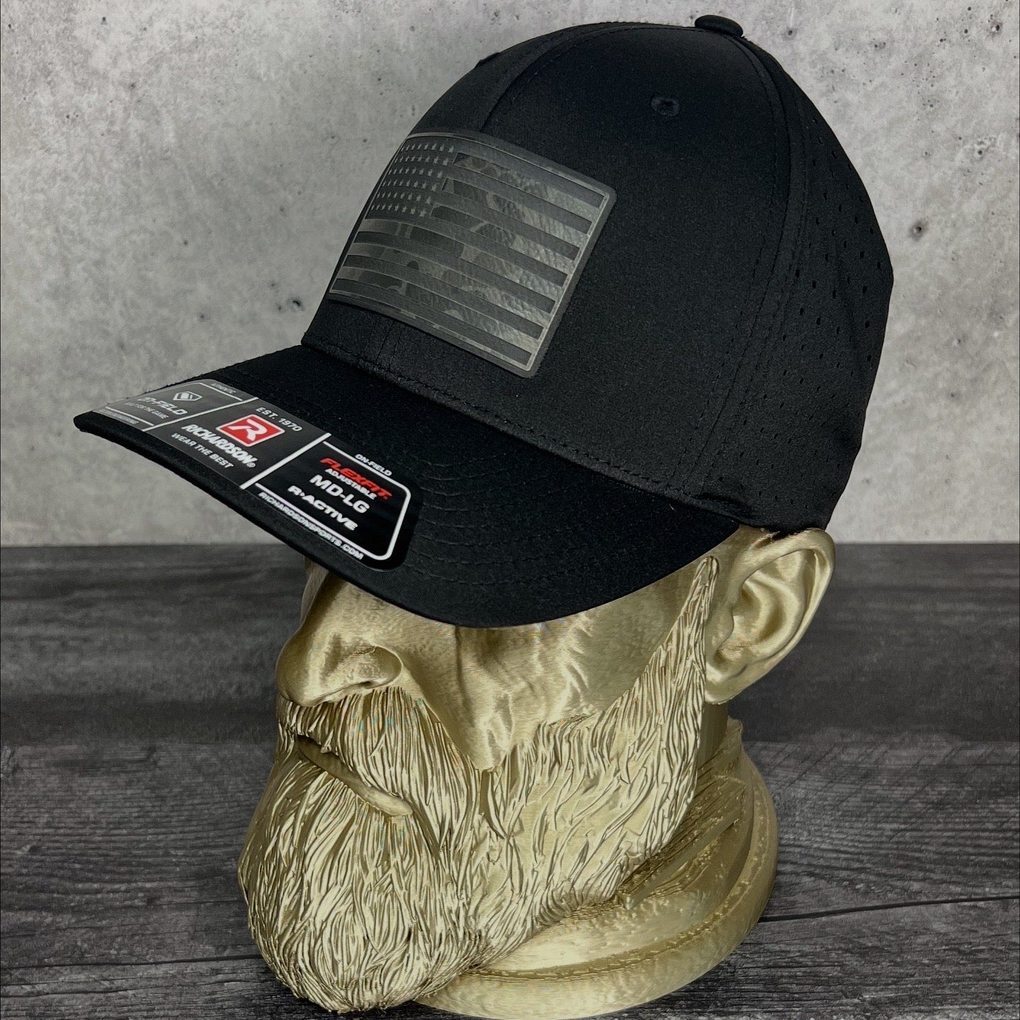 Black cap with patches on a mannequin head against a concrete wall.