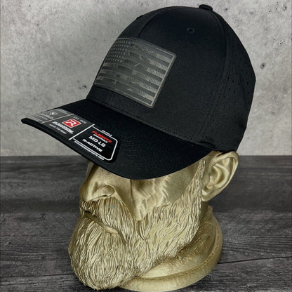 Black cap with patches on a mannequin head against a concrete wall.
