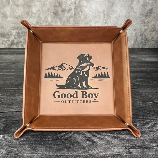 Brown leather tray with 'Good Boy Outfitters' logo on a textured surface