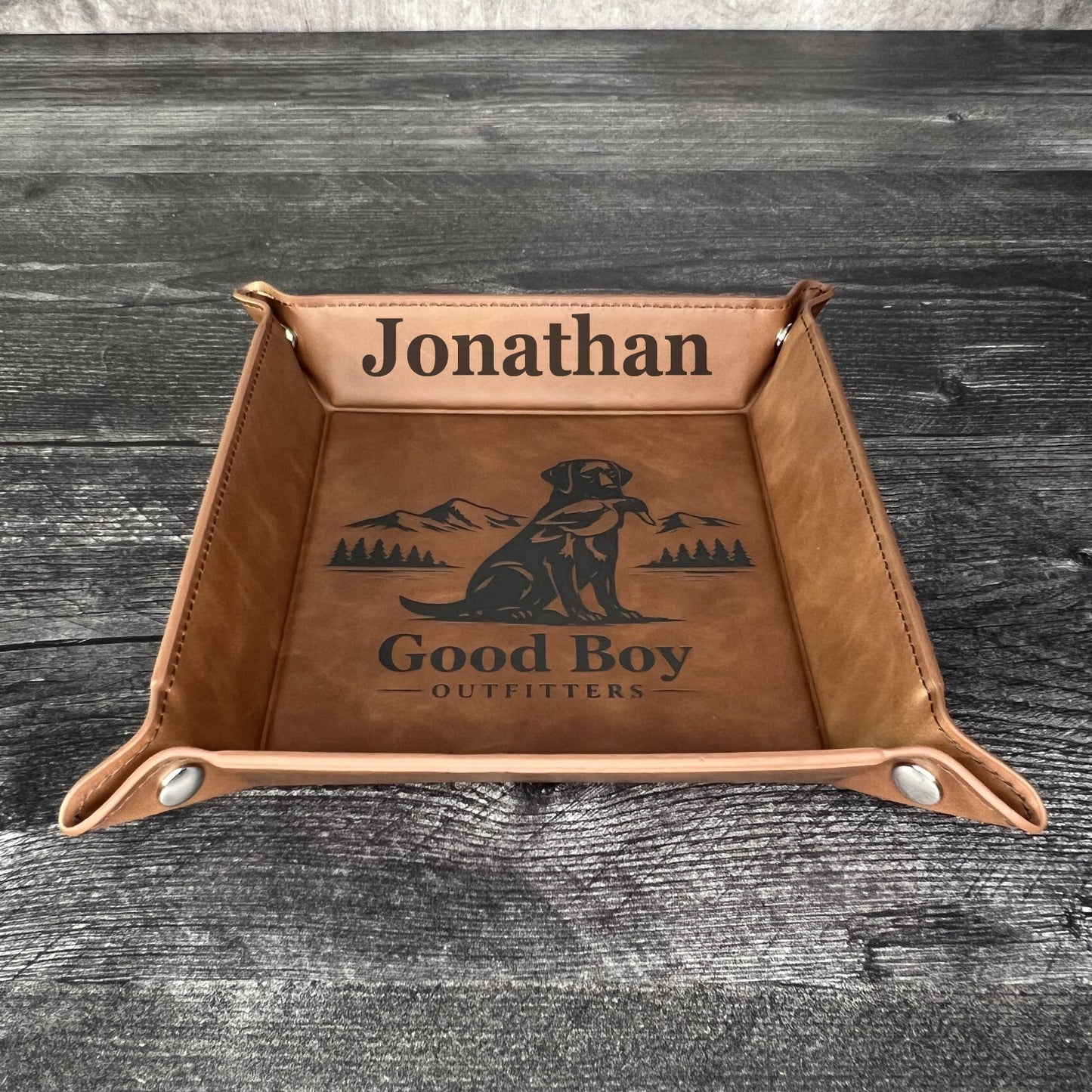 Brown leather tray with engraved text and logo on a wooden surface