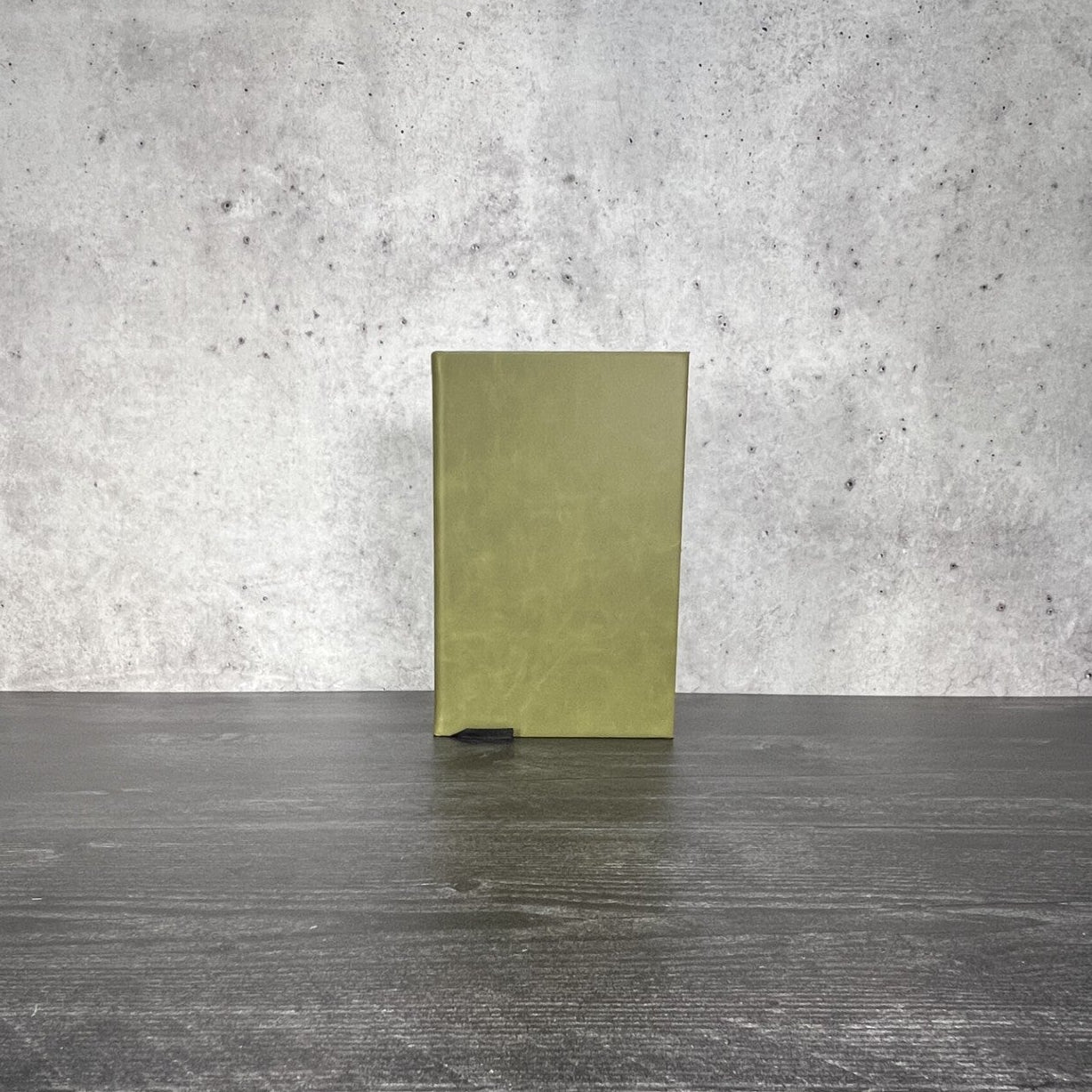 Olive leatherette journal on a wooden floor with a concrete wall