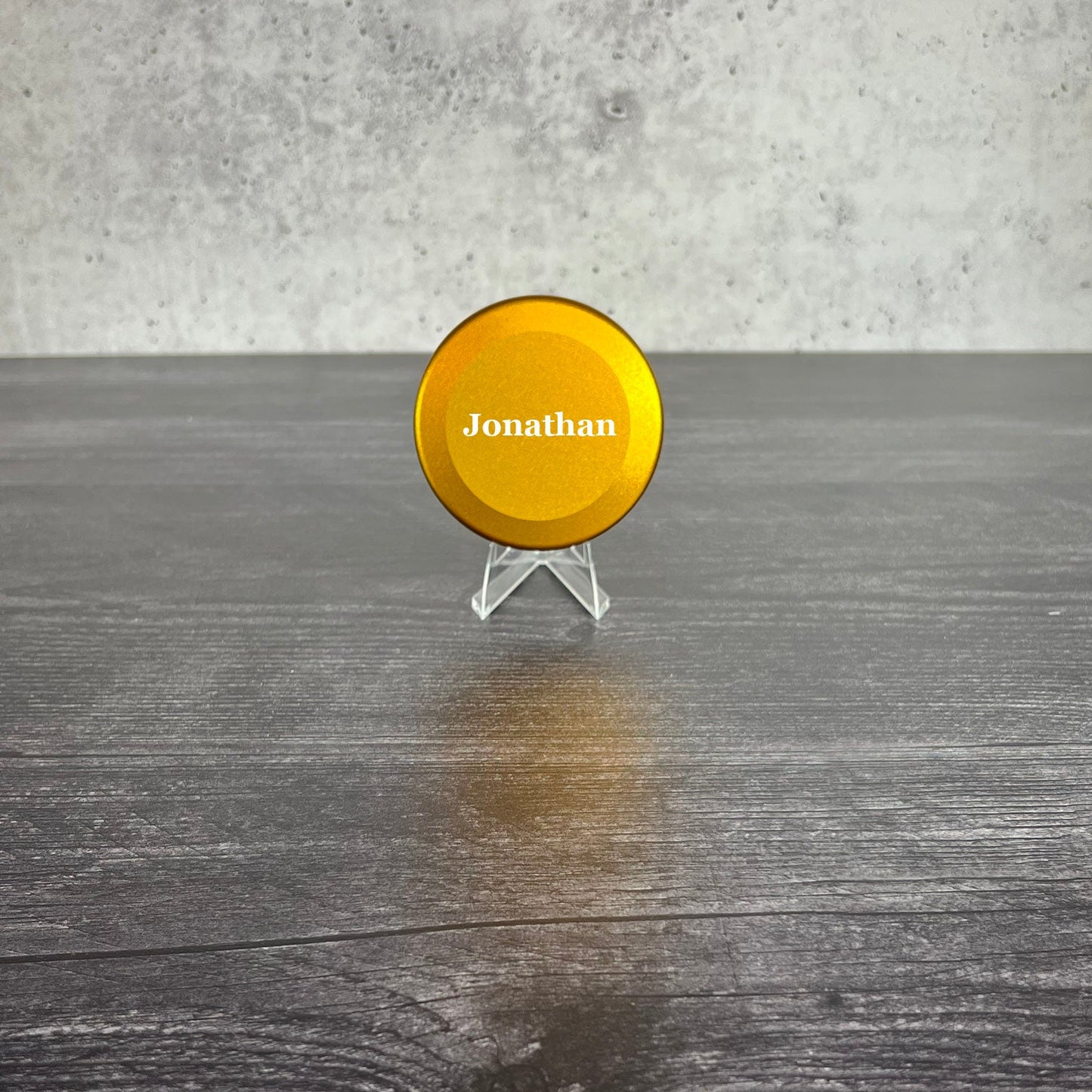 Yellow disc with 'Jonathan' on a stand against a gray concrete wall.