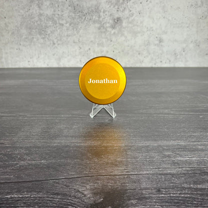 Yellow disc with 'Jonathan' on a stand against a gray concrete wall.