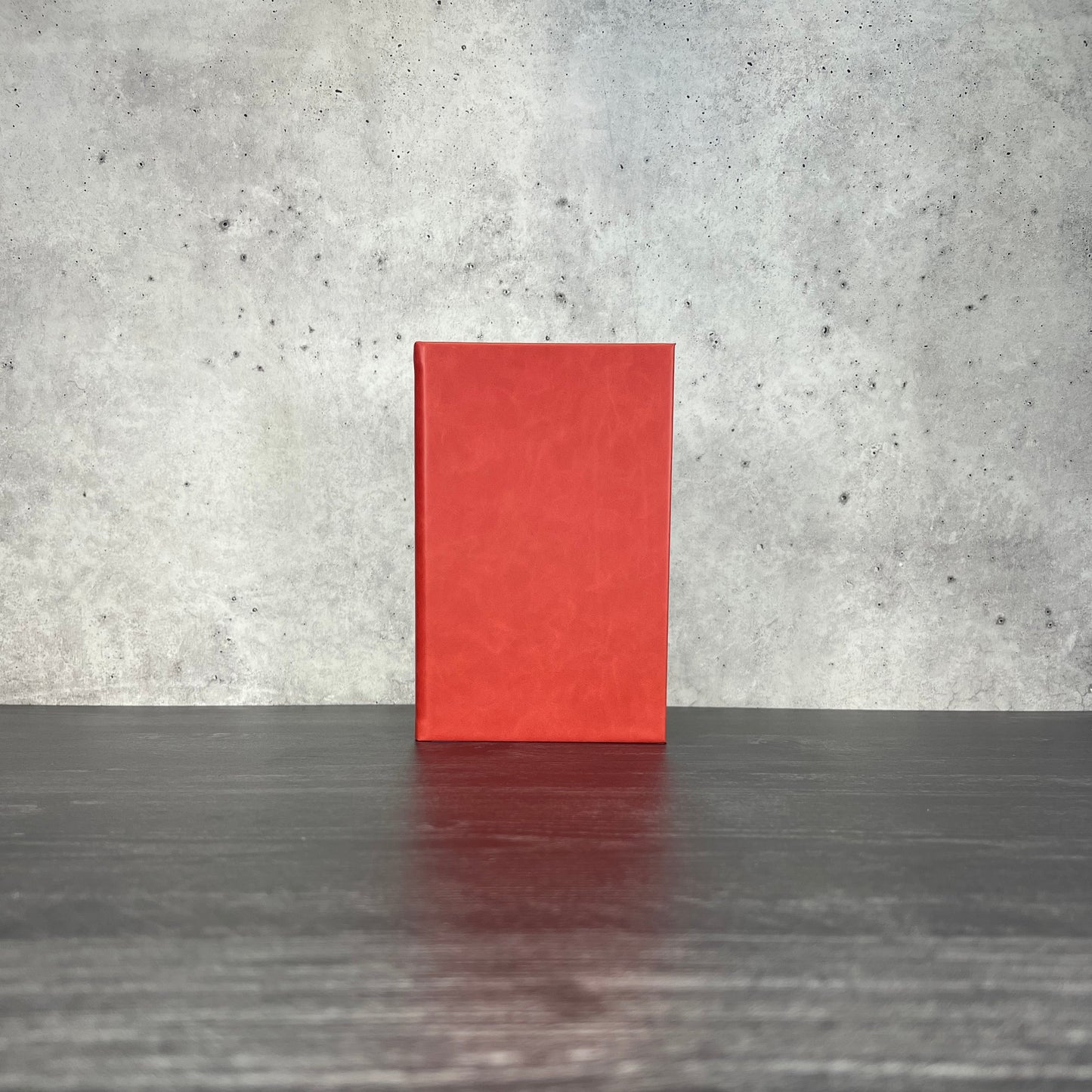 Red leatherette journal on a wooden floor with a concrete wall