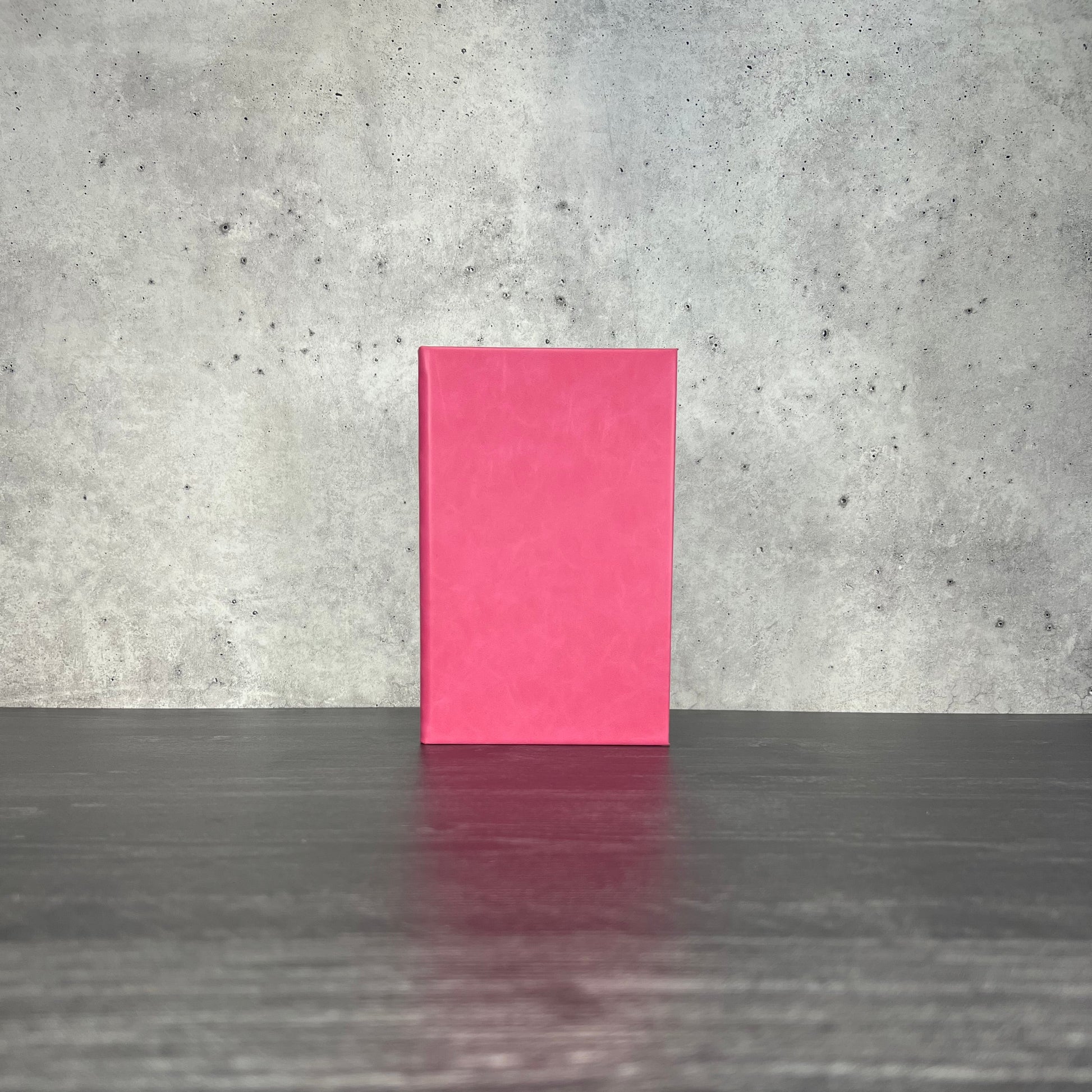 Pink leatherette journal on a wooden floor with a concrete wall