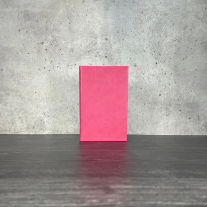 Pink leatherette journal on a wooden floor with a concrete wall