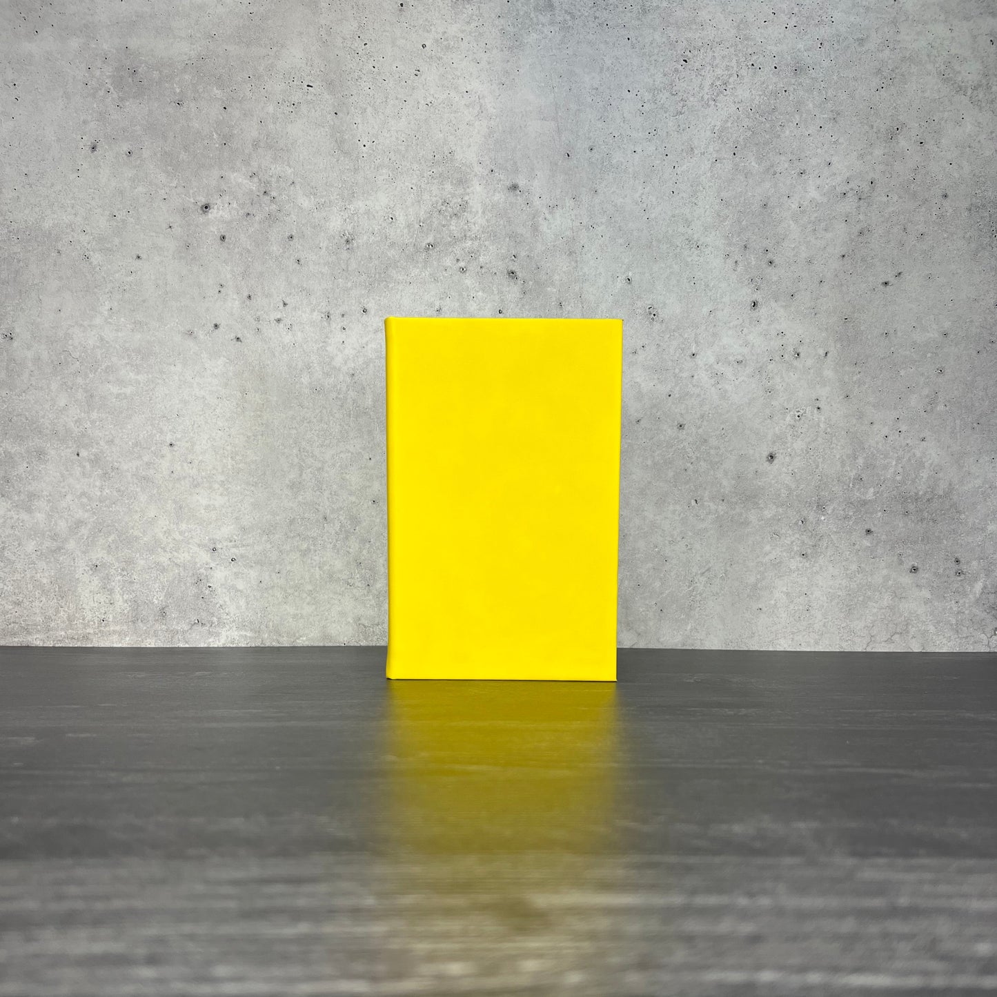 Yellow leatherette journal on a wooden floor with a concrete wall