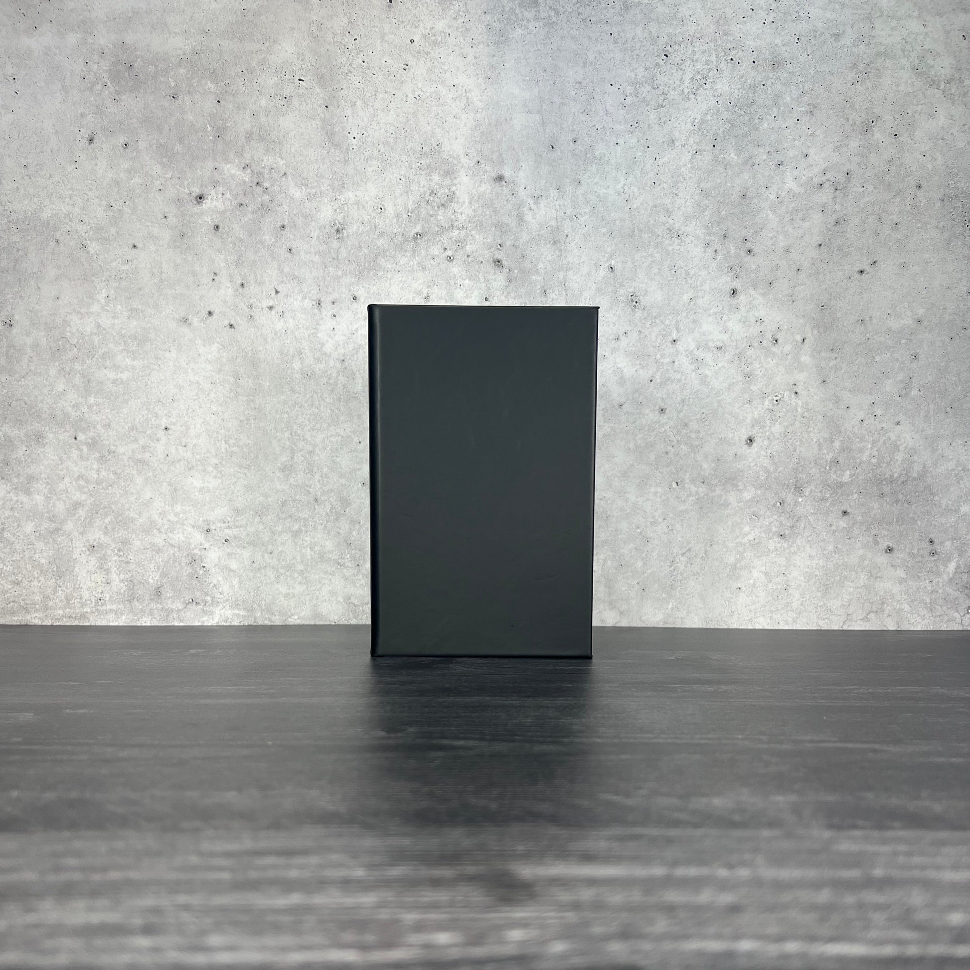 Black leatherette journal on a wooden floor with a concrete wall