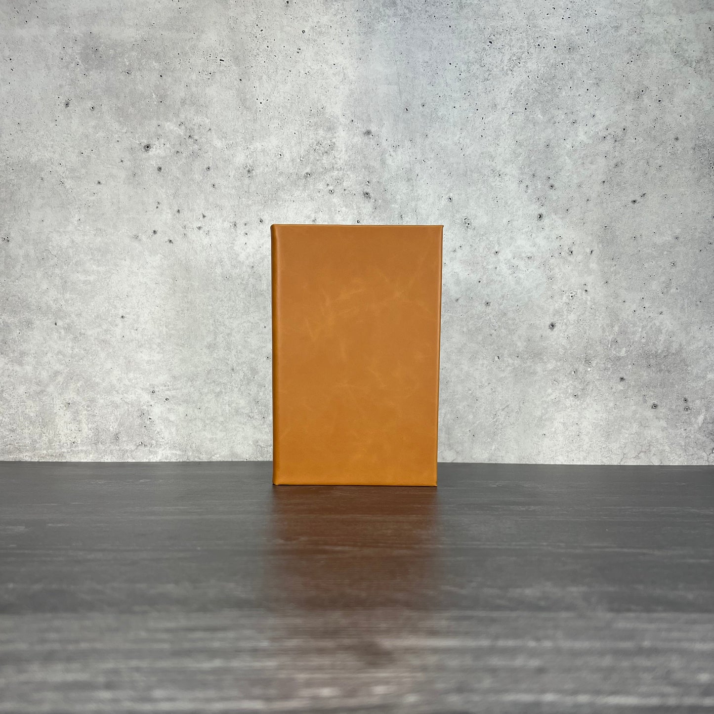 Raw leatherette journal on a wooden floor with a concrete wall