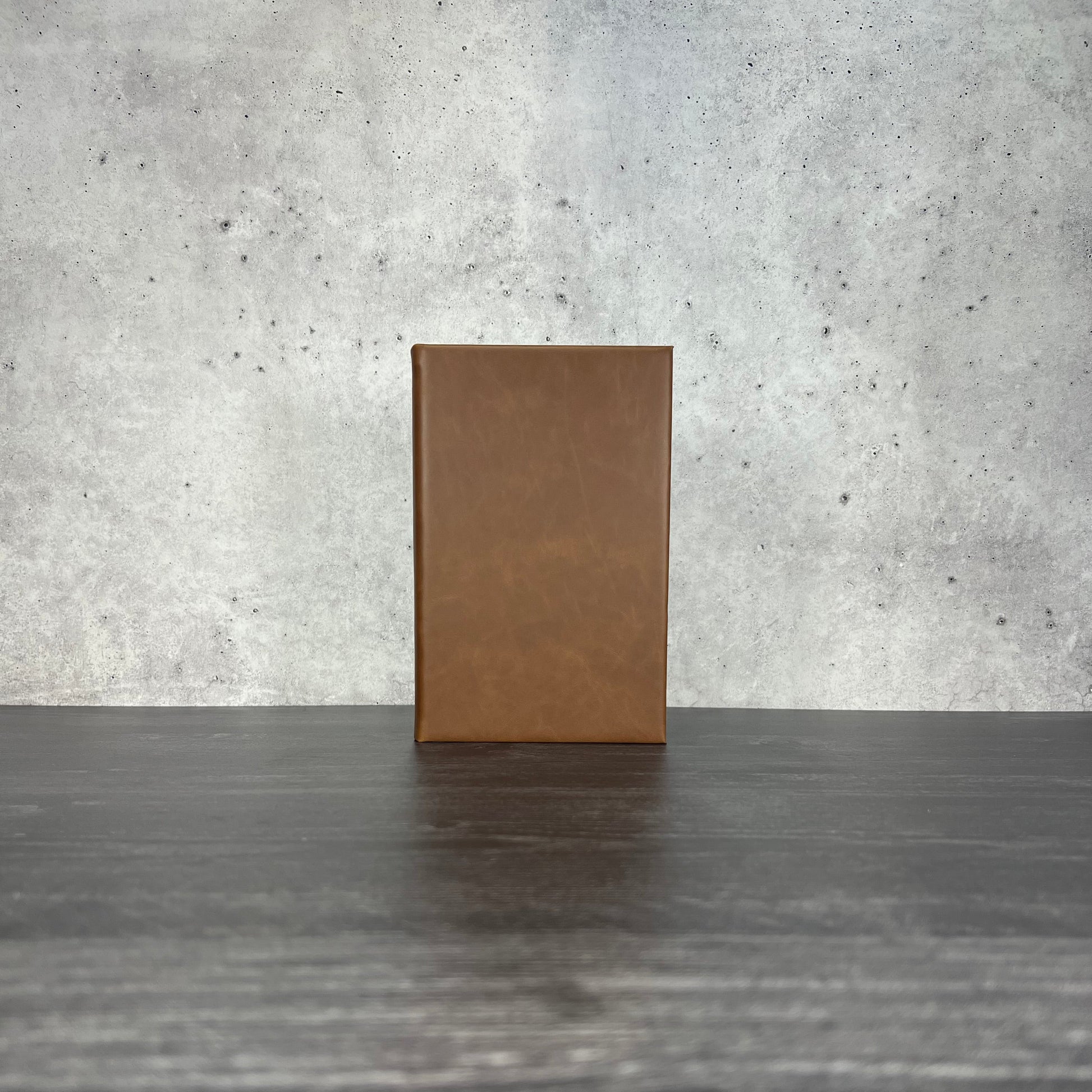 Walnut leatherette journal on a wooden floor with a concrete wall