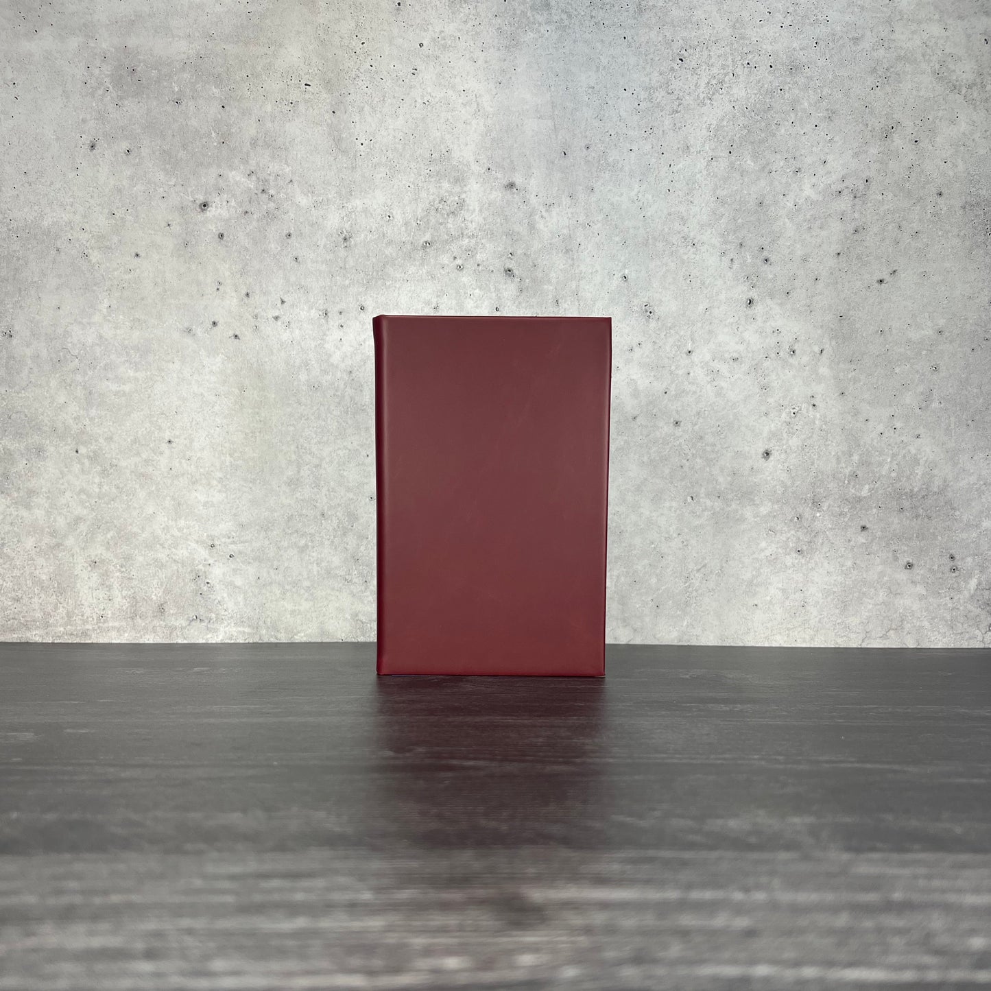 Crimson leatherette journal on a wooden floor with a concrete wall