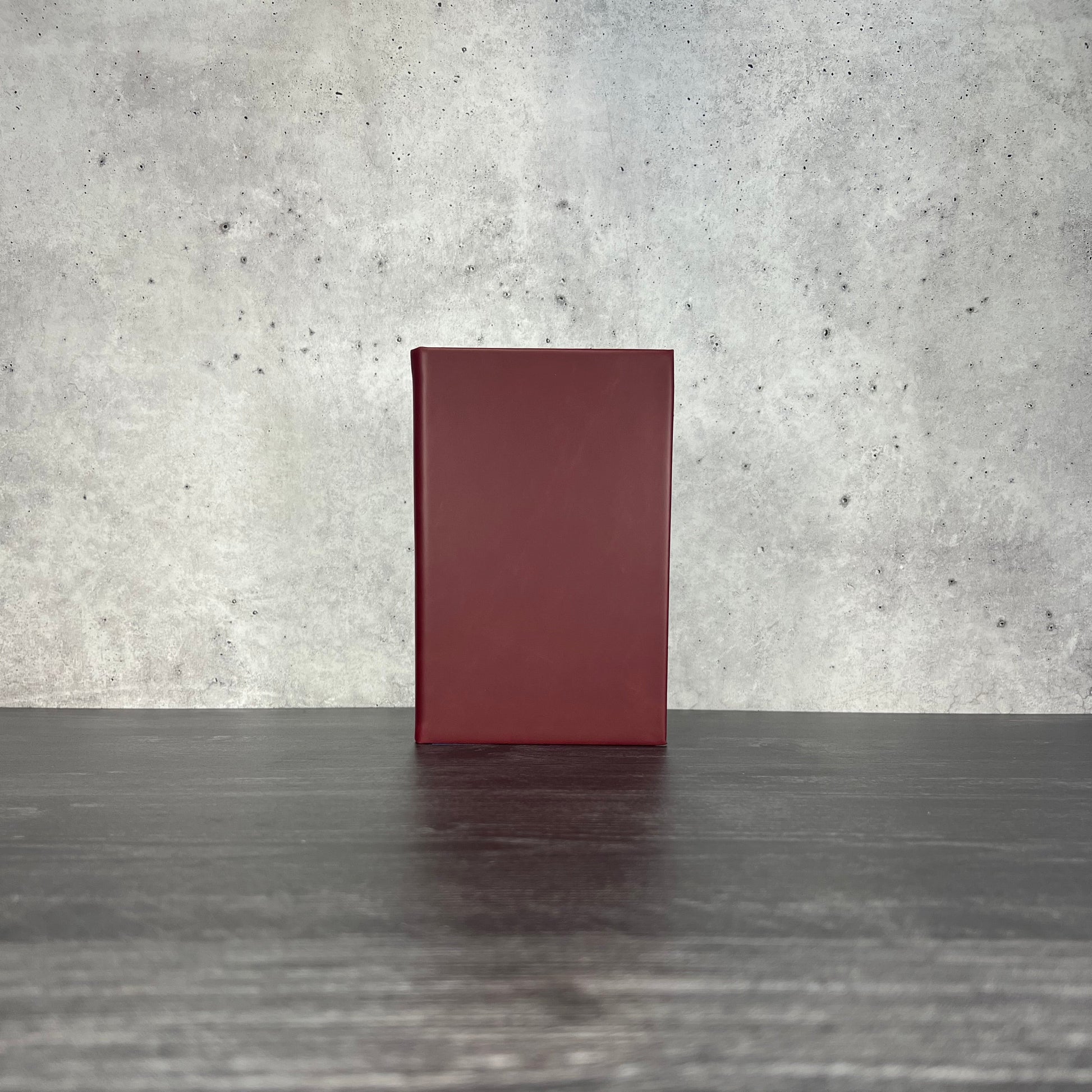Crimson leatherette journal on a wooden floor with a concrete wall