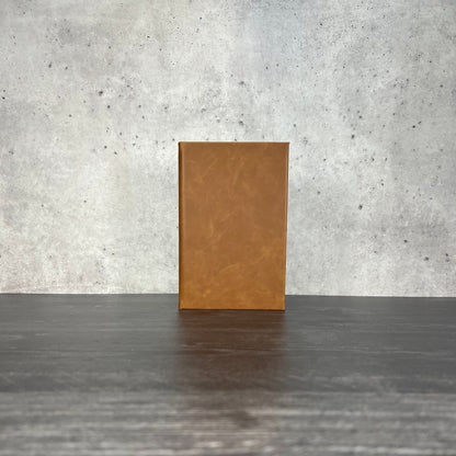 Buckskin leatherette journal on a wooden floor with a concrete wall