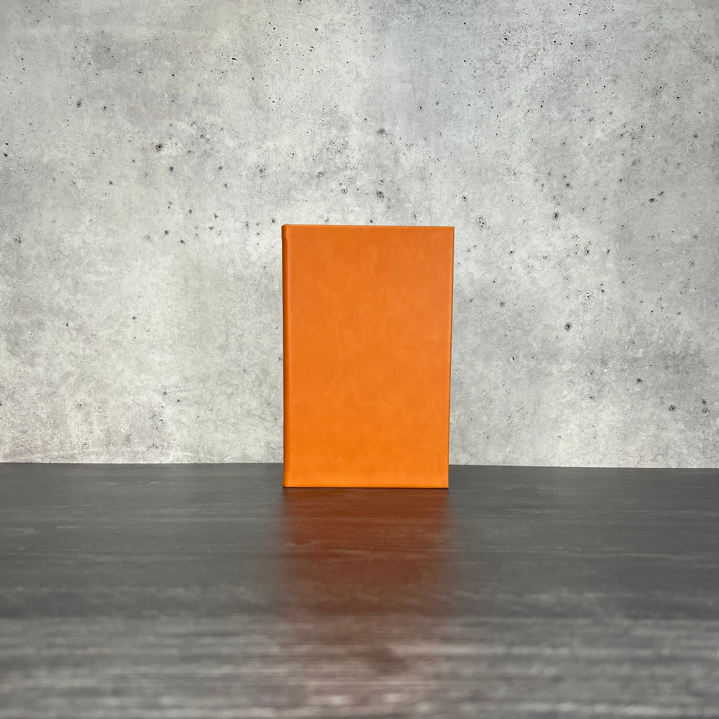 Orange leatherette journal on a wooden floor with a concrete wall