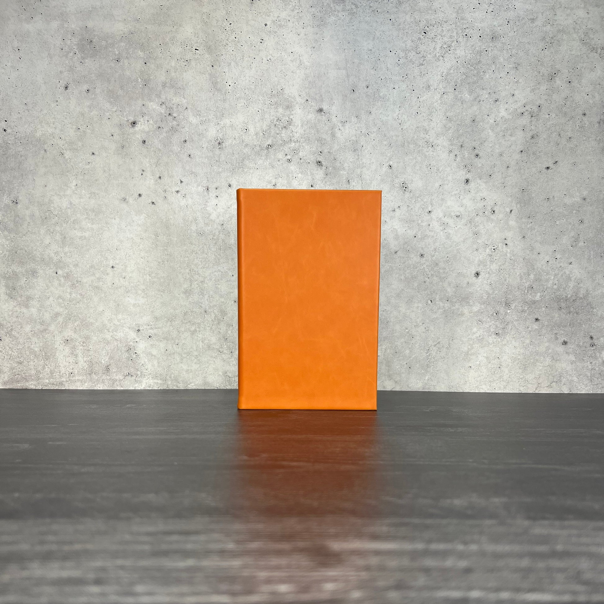 Orange leatherette journal on a wooden floor with a concrete wall
