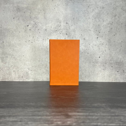 Orange leatherette journal on a wooden floor with a concrete wall