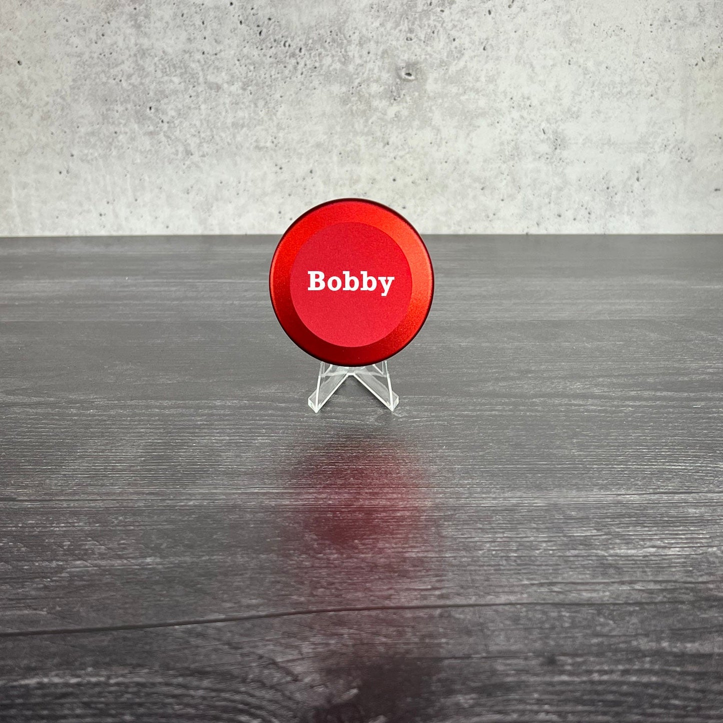 Red circular sign with 'Bobby' on a stand against a gray concrete wall.