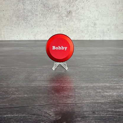 Red circular sign with 'Bobby' on a stand against a gray concrete wall.