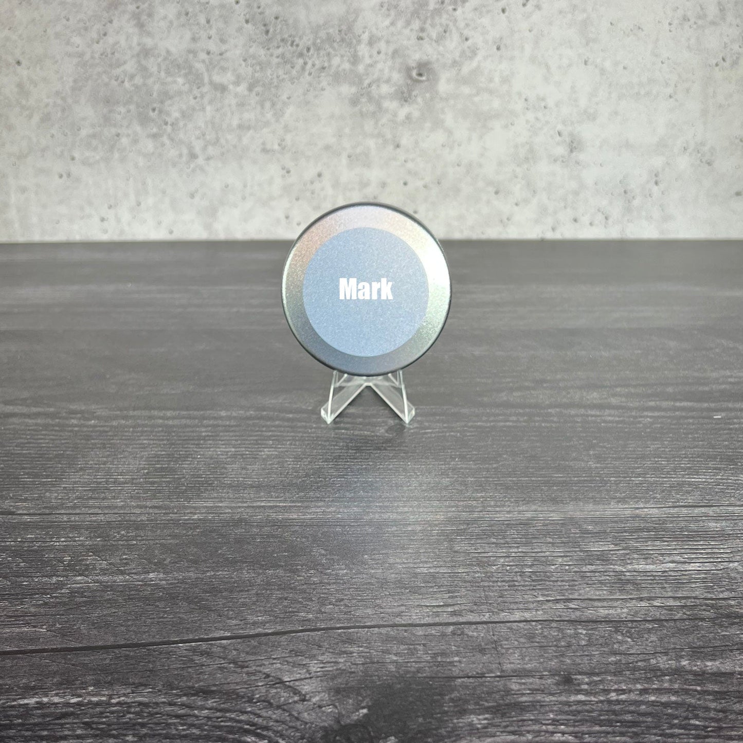 Round metallic object with 'Mark' engraved on it, placed on a wooden surface.