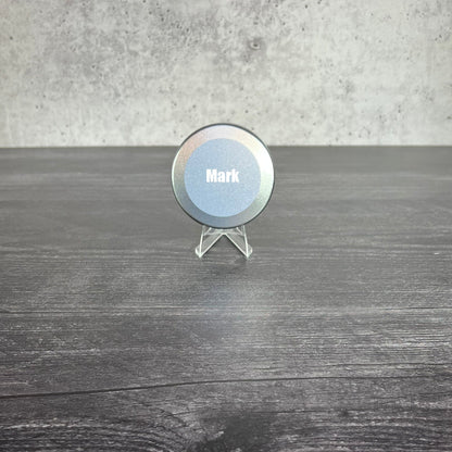 Round metallic object with 'Mark' engraved on it, placed on a wooden surface.
