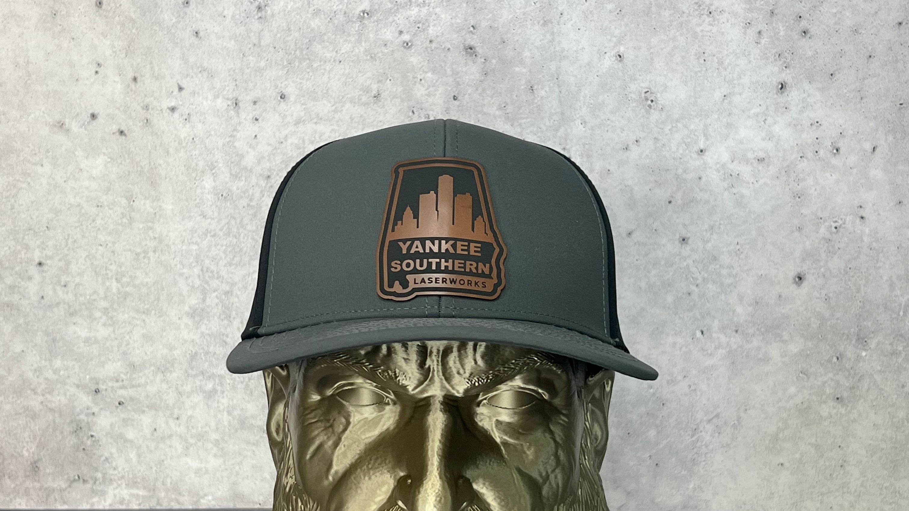 Yankee Southern Laserworks 6 panel hat with walnut colored branded patch on a gold statue.